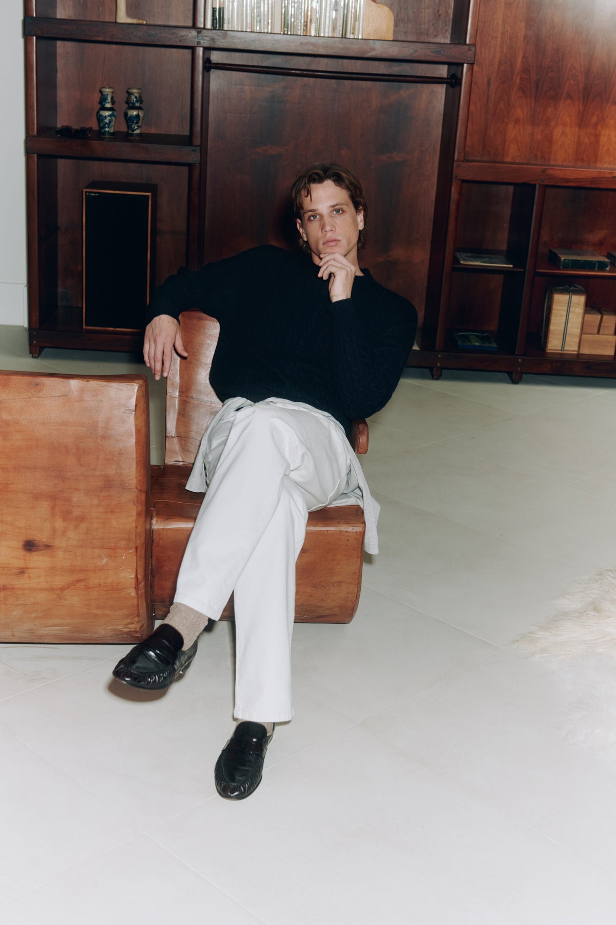 Model in a dark polo and pale trousers seated by wood cabinetry